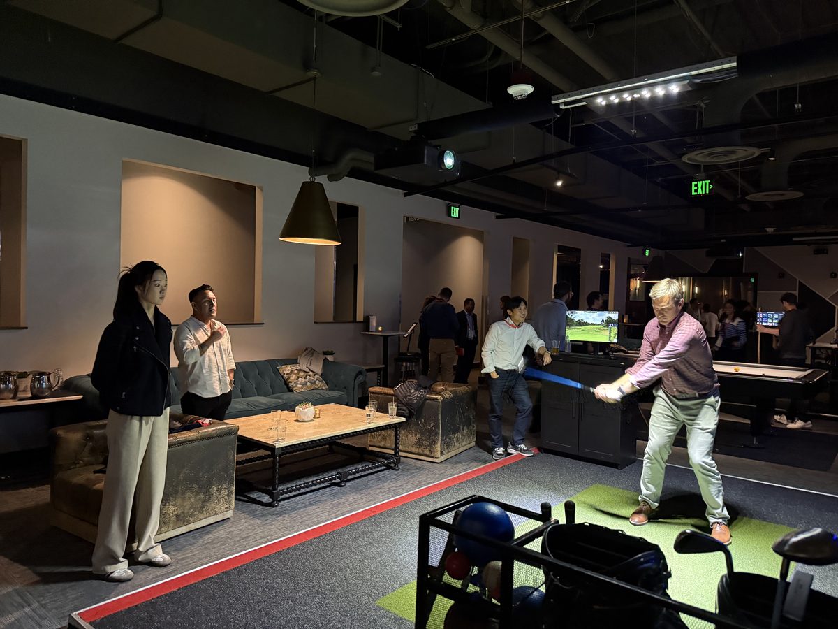 Lab member swinging at an indoor golf simulator while others watch